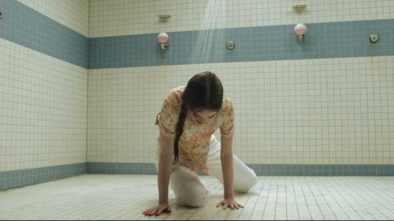 Young girl played by Summer H. Howell crouches on shower floor in high school gym in Carrie TV show