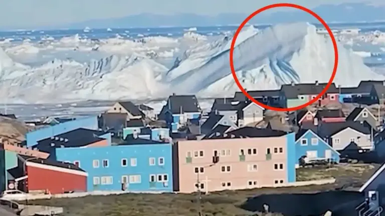 Gran iceberg de hielo azulado frente a las casas de colores del poblado costero de Ilulissat en Groenlandia