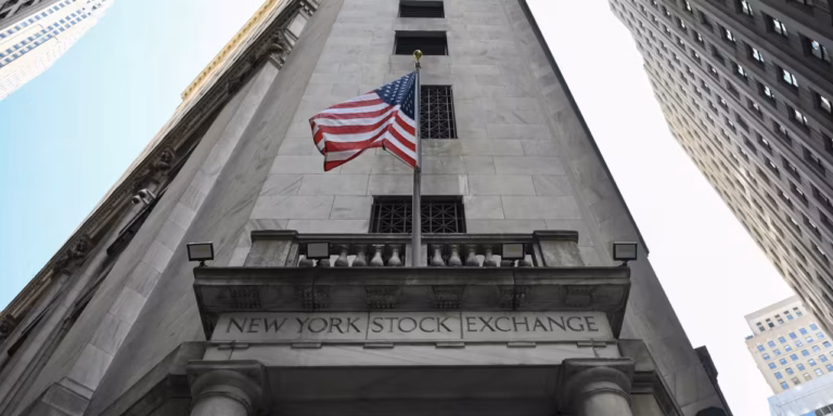View of the New York Stock Exchange building with an American flag flying, surrounded by other tall buildings