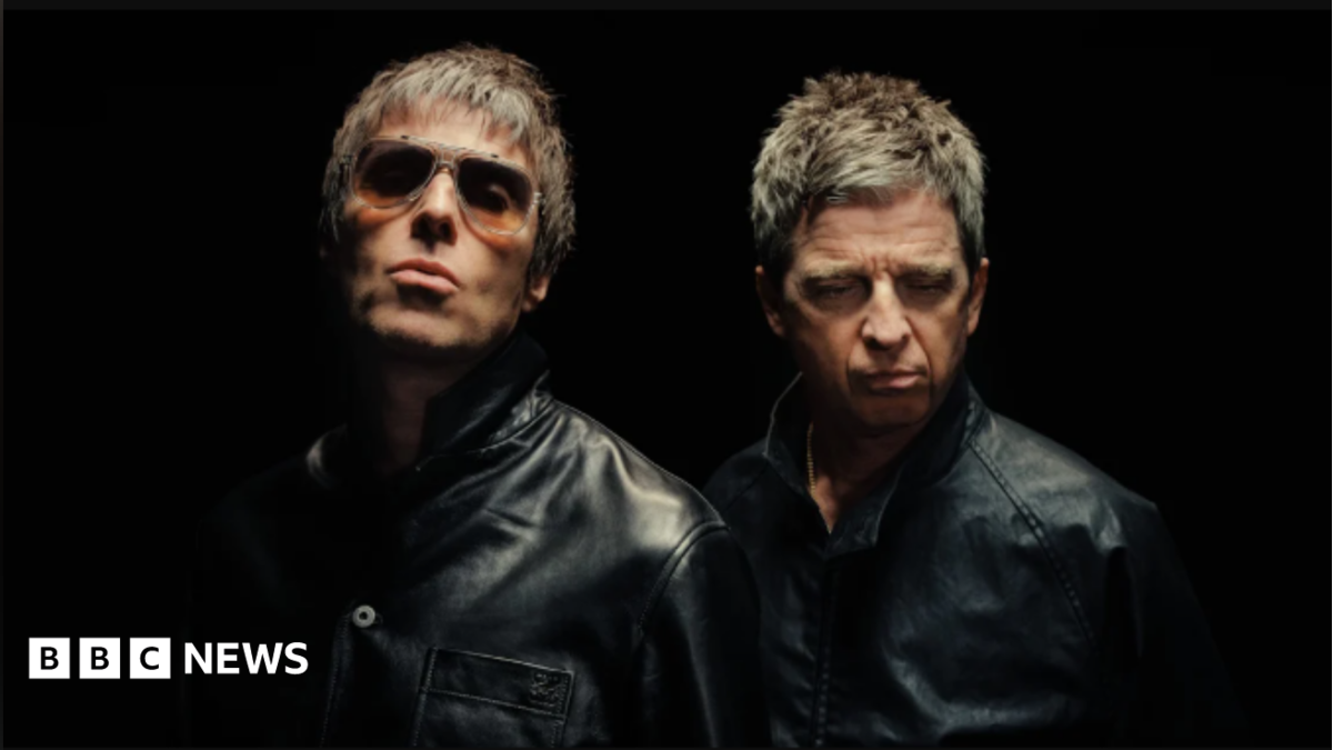 Liam and Noel Gallagher, both wearing black and looking serious in front of a black backdrop. Liam is wearing sunglasses