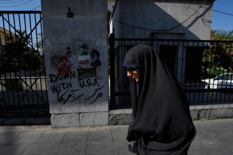 A woman walks past anti-U.S. graffiti and images depicting the late Iranian Supreme Leader Ayatollah Ali Khamenei painted on