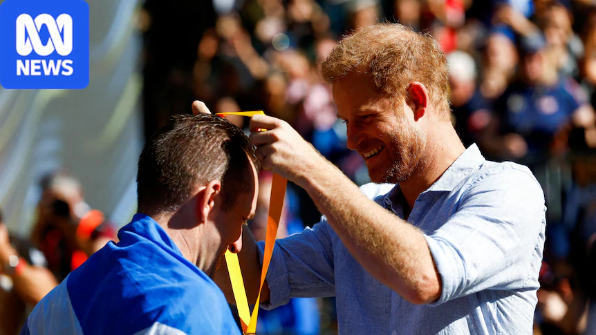A man with orange hair wearing a blue shirt puts a medal around the neck of a man facing him in a blue and white tracksuit