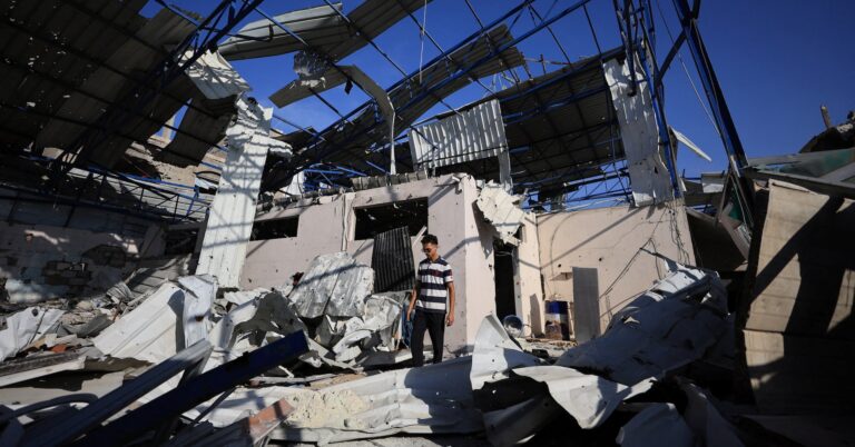 A Palestinian young man stands amid the debris of Al-Hassayna family’s company warehouse, damaged during the war, in Gaza