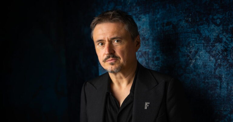 A man in black stands against a dark blue backdrop