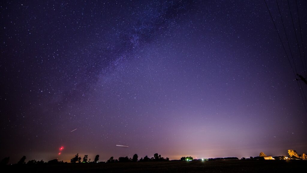 Draconid meteors streak across the night sky. The Milky Way can also be seen stretching across the star-studded sky